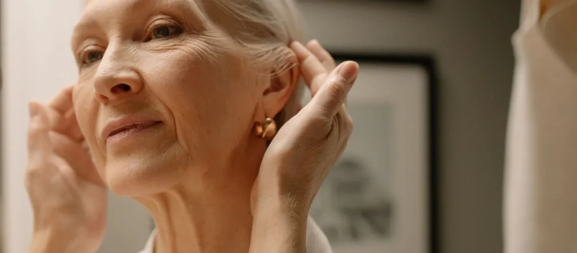 Femme âgée ajustant ses boucles d'oreilles devant un miroir.
