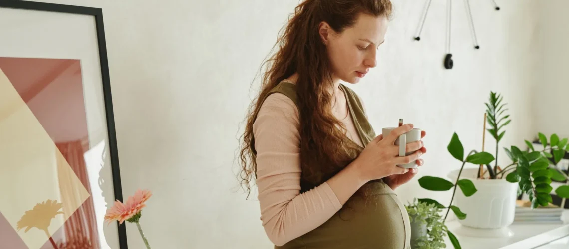 Scène intérieure cosy d'une femme enceinte tenant une tasse entourée de plantes.