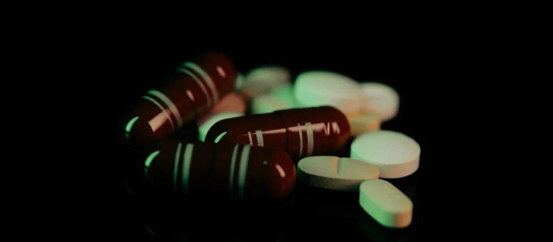 Comprimés et gélules variés sous une lumière verte sur fond sombre, représentant les produits pharmaceutiques.