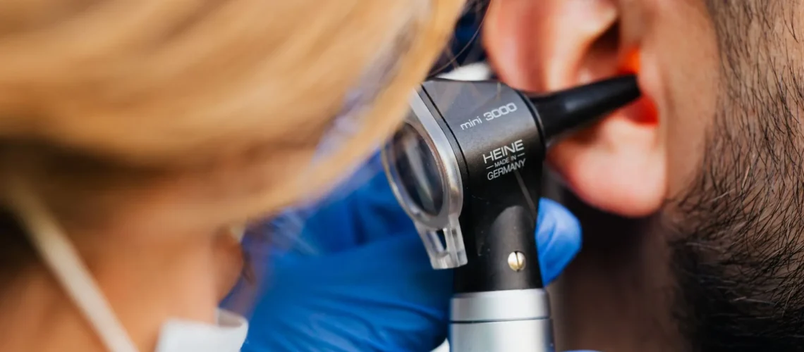 Un professionnel de santé examine l'oreille d'un patient à l'otoscope Heine, illustrant la qualité des soins.