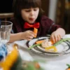 Enfant en nœud papillon rouge savourant un repas sain avec des légumes à l'intérieur.