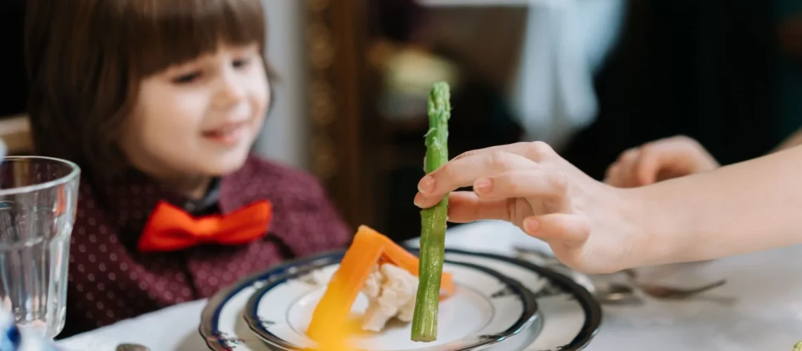 Enfant avec un nœud papillon assis à table profitant d'une expérience gastronomique avec des aliments sains