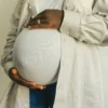 Femme enceinte en tenue décontractée tenant doucement son ventre, symbolisant la maternité