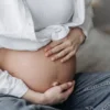 Gros plan sur une femme enceinte assise, berçant son ventre nu avec ses deux mains.