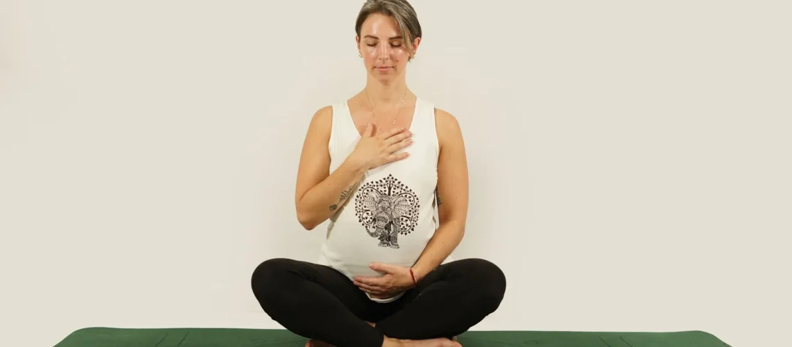 Femme enceinte méditant en tailleur sur un tapis de yoga vert