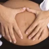 Gros plan d'un ventre de femme enceinte avec des mains formant un cœur, symbolisant l'amour et la maternité.