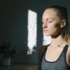 Une femme méditant dans une pièce ensoleillée, les yeux fermés, ressentant calme et paix.