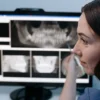 Une dentiste examine des radiographies dentaires numériques sur un écran d'ordinateur dans une clinique.