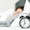Un réveil rétro posé près d'une femme endormie dans une chambre confortable.