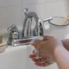 Mains se lavant sous un robinet avec de l'eau courante, soulignant l'hygiène et la propreté.