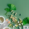 Vue à plat de compléments et médicaments variés avec des feuilles de ginkgo sur fond vert, illustrant le concept de remède naturel