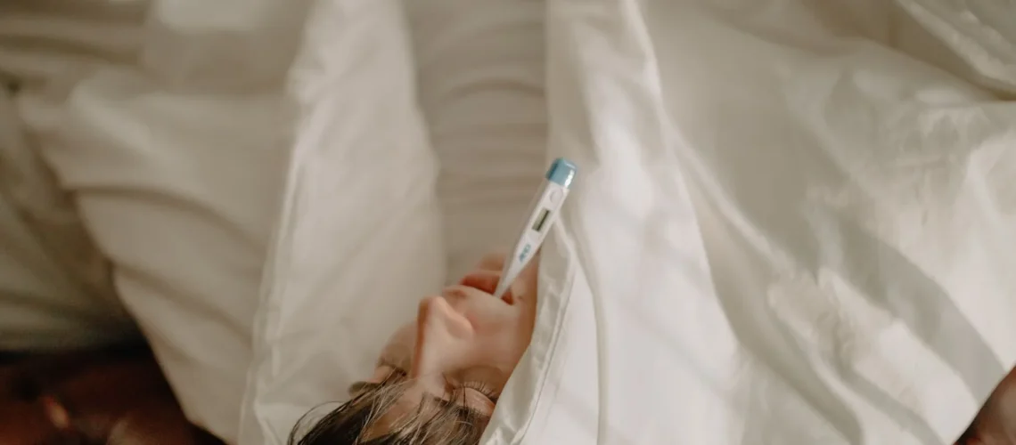 Un homme alité avec un thermomètre dans la bouche, emmitouflé dans une couette, indiquant une maladie ou de la fièvre