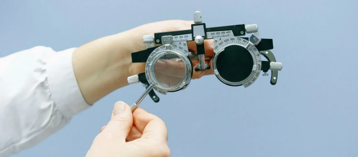 Ophtalmologiste anonyme réglant des lunettes de test de vision avec une loupe et une échelle numérique sur fond bleu.