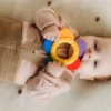 Un bébé mignon mâche un jouet de dentition coloré allongé sur une surface douce.