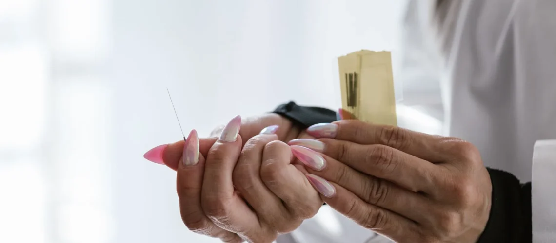 Gros plan sur les mains d'un acupuncteur tenant délicatement des aiguilles d'acupuncture.