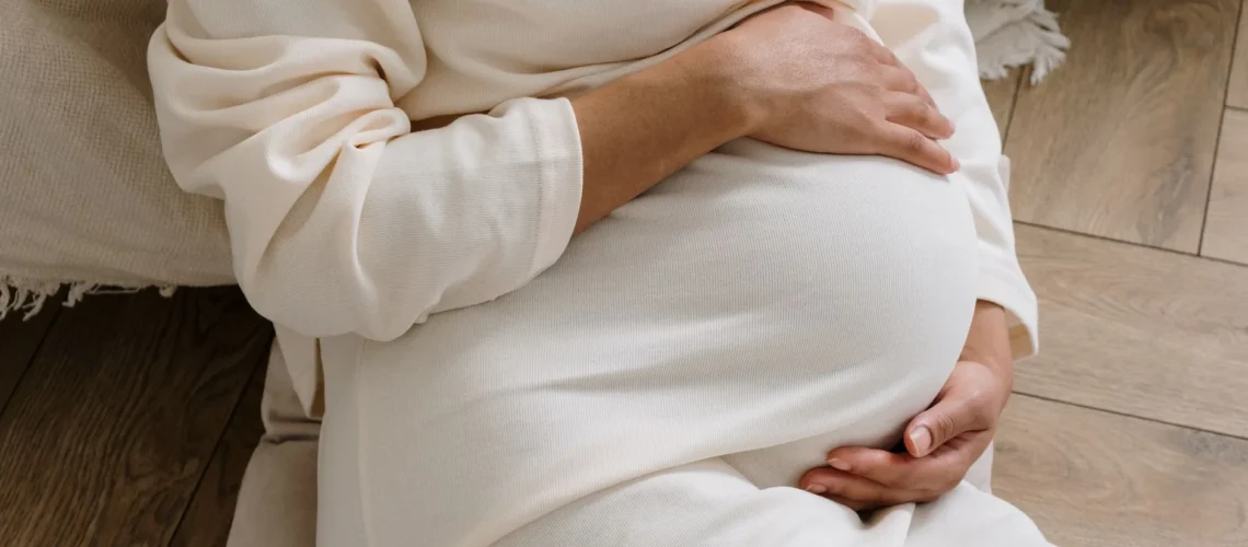 Un moment serein d'une femme enceinte dans une robe blanche confortable tenant son ventre.