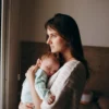 Un moment serein : une mère tenant son bébé endormi près d'une fenêtre, à l'intérieur