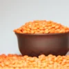 Un bol rempli de lentilles corail bien rouges sur un fond uni.