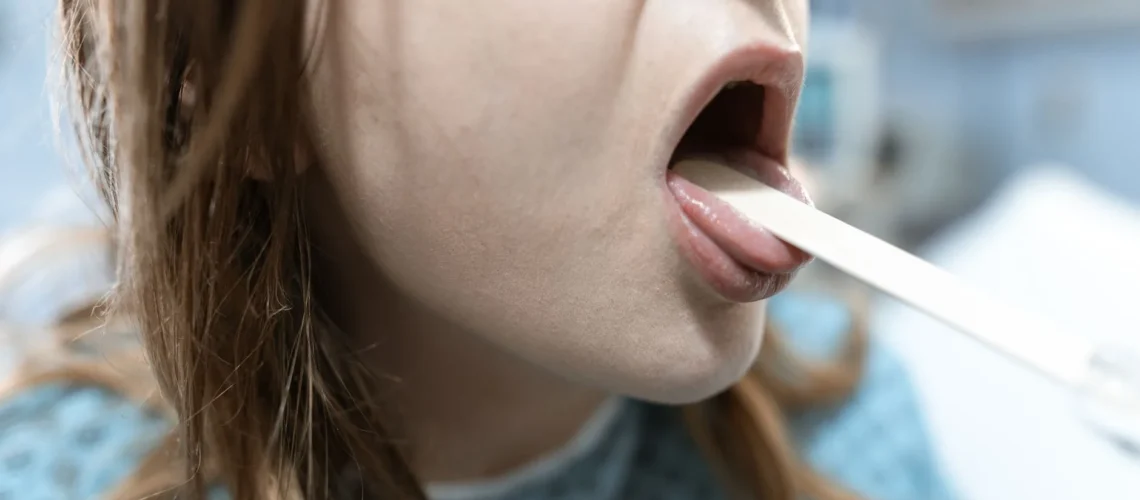 Gros plan sur une femme se faisant examiner la gorge en milieu médical avec un abaisse-langue.
