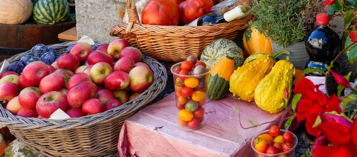 Étal de fruits et légumes frais sur un marché de plein air : pommes, tomates, courges et herbes aromatiques.