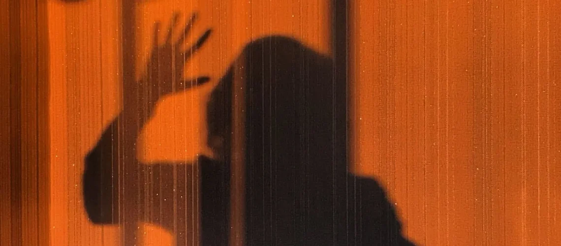Ombre étrange d'une personne sur un mur orange créant une ambiance mystérieuse