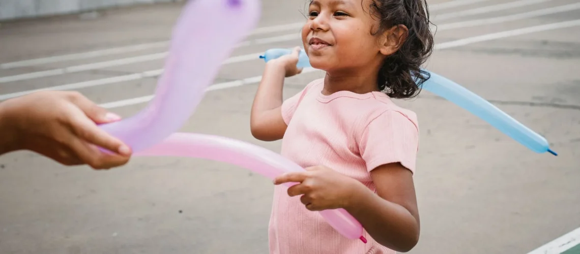 Enfant souriant jouant avec des ballons colorés dehors dans une aire de jeux