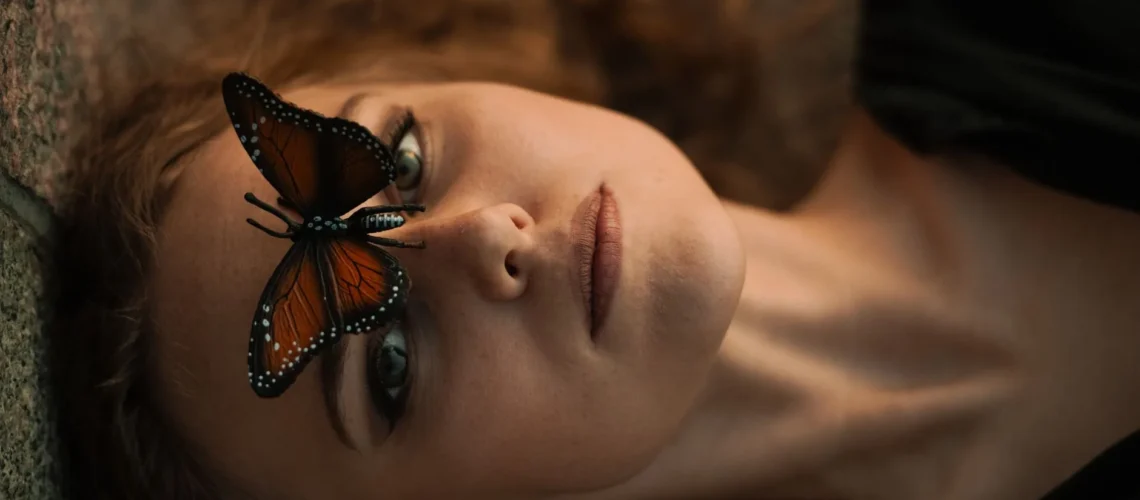 Gros plan d'une femme avec un papillon monarque posé sur son visage, évoquant la sérénité.