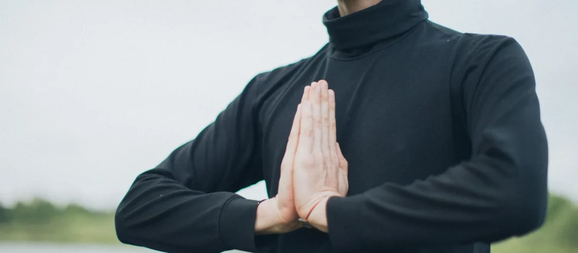 Gros plan d'une personne méditant en extérieur, mains en position de prière, pour le bien-être.
