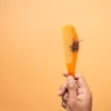 Gros plan sur une main tenant un peigne avec des cheveux sur fond orange, illustrant la perte de cheveux.