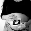 Une femme enceinte tient une échographie contre son ventre, symbolisant l'attente de la maternité.