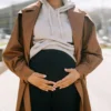 Une femme enceinte élégante, les mains sur le ventre, dans un environnement urbain moderne.