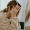 Femme assise à l'intérieur se couvrant le visage de frustration, dépeignant le stress et les défis de santé mentale