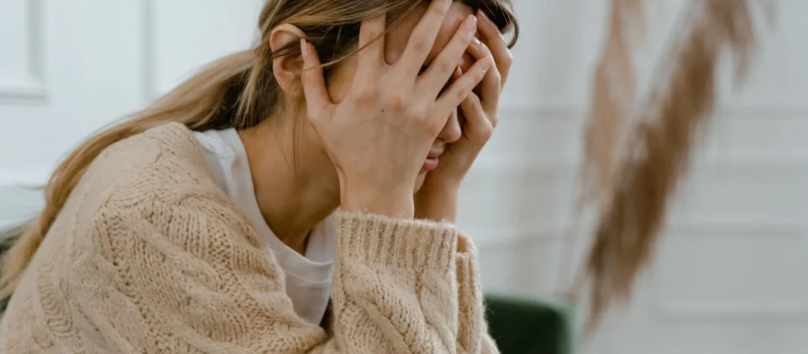 Femme assise à l'intérieur se couvrant le visage de frustration, dépeignant le stress et les défis de santé mentale