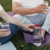 Un couple se détend en plein air sur des tapis de yoga, tenant des verres d'eau, promotion de l'hydratation et du bien-être
