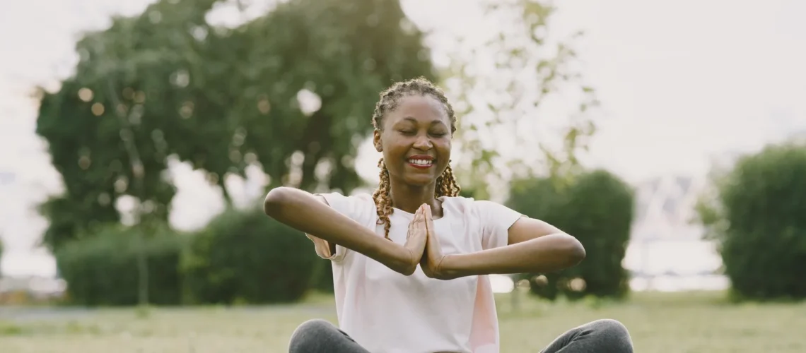 Femme afro-américaine pratiquant le yoga dans un parc ensoleillé, profitant de la relaxation et du bien-être en plein air.