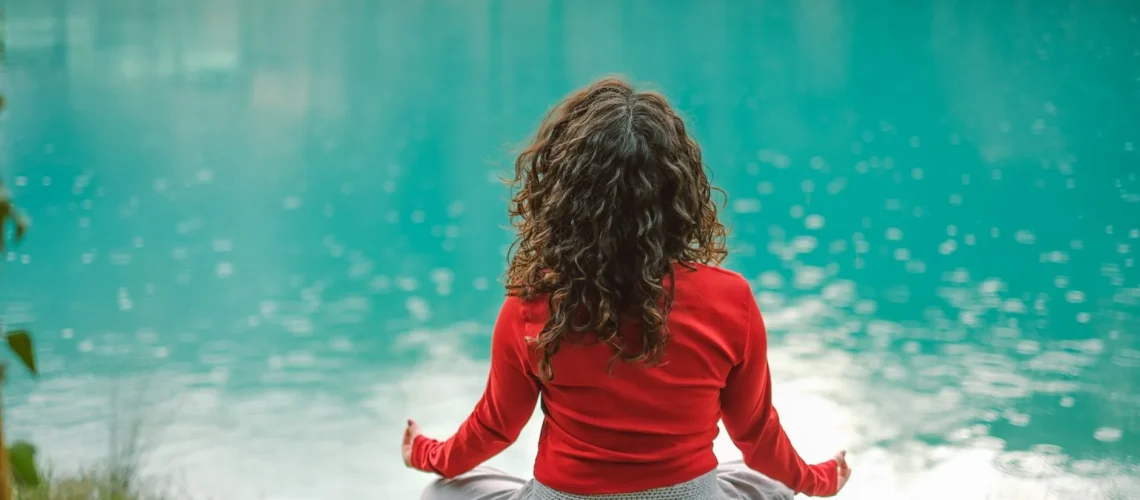 Femme en rouge méditant au bord d'un lac bleu tranquille, reflétant calme et sérénité