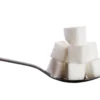 Morceaux de sucre empilés sur une cuillère sur fond blanc, évoquant simplicité et douceur.