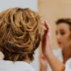 Vue de dos d'une femme coiffant ses cheveux courts devant un miroir.