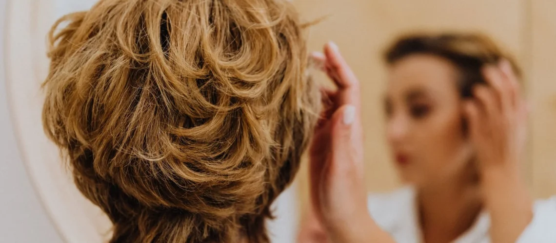 Vue de dos d'une femme coiffant ses cheveux courts devant un miroir.