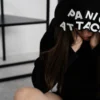 Une femme assise avec « PANIC ATTACK » sur sa capuche, montrant de l'anxiété en intérieur.