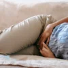 Femme non identifiée en tenue décontractée allongée sur un canapé, souffrant d'une douleur aiguë à l'estomac.