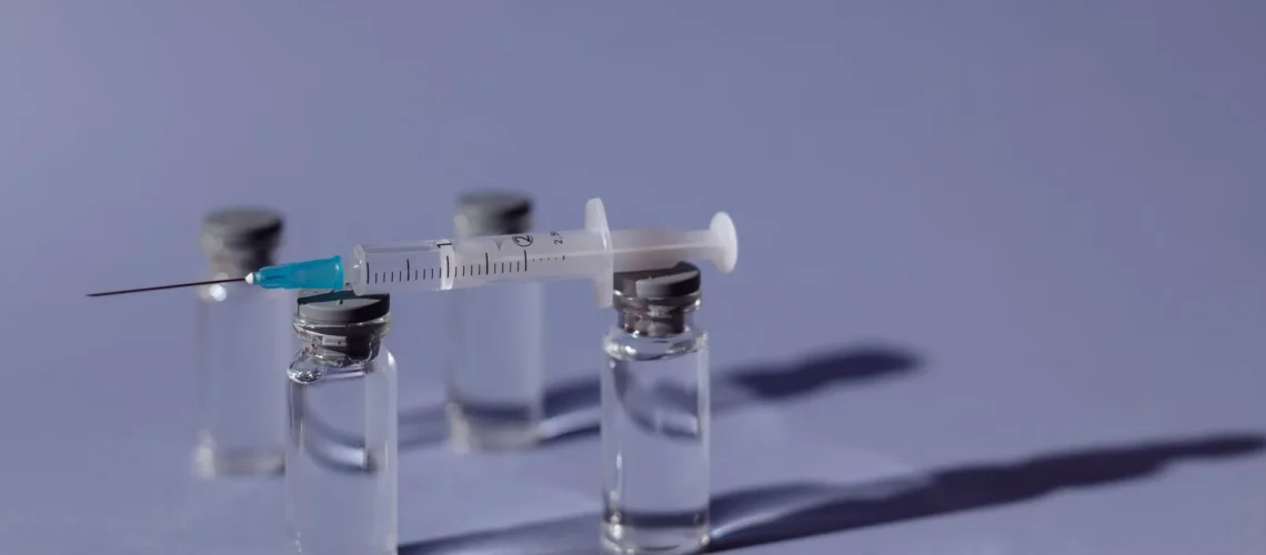 Une seringue en équilibre sur des flacons de vaccin avec un fond violet, représentant un traitement médical.