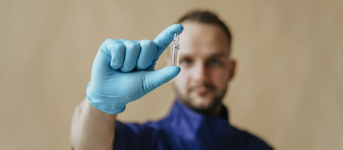 Un professionnel de santé masculin en gants de protection tenant un petit flacon, axé sur la recherche médicale et la sécurité.