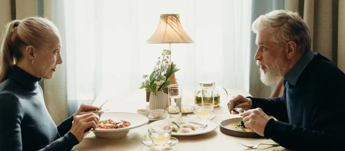 Un couple âgé partage un repas dans un cadre intérieur chaleureux et douillet.