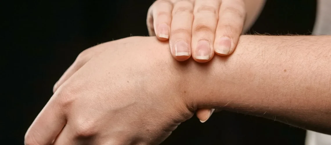 Gros plan sur les mains d'une personne pressant son poignet, mettant l'accent sur la peau et sa texture.
