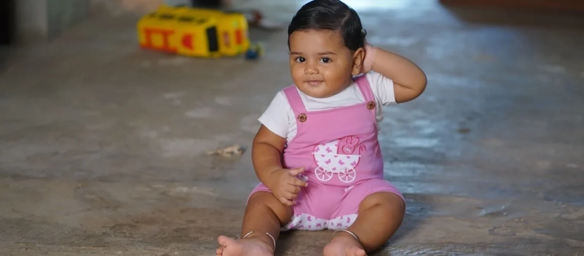 Bébé charmant en salopette rose assis à l'intérieur avec un jouet sur un sol en béton