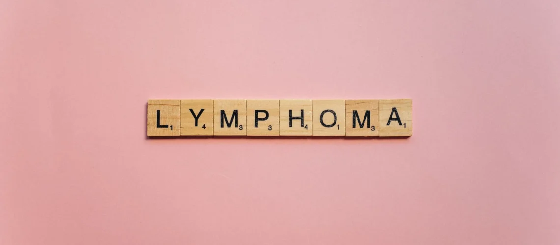 Lettres en bois formant le mot « Lymphome » sur fond rose, symbolisant la sensibilisation.