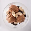 Vue de dessus en gros plan d'un mélange de noix, noix de cajou et graines de courge dans un bol en verre.