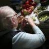 Femme âgée épluchant des légumes dans une cuisine chaleureuse, entourée de produits frais.