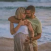 Un couple amoureux s'enlace sur une plage sereine, mettant en avant l'intimité et l'attente.